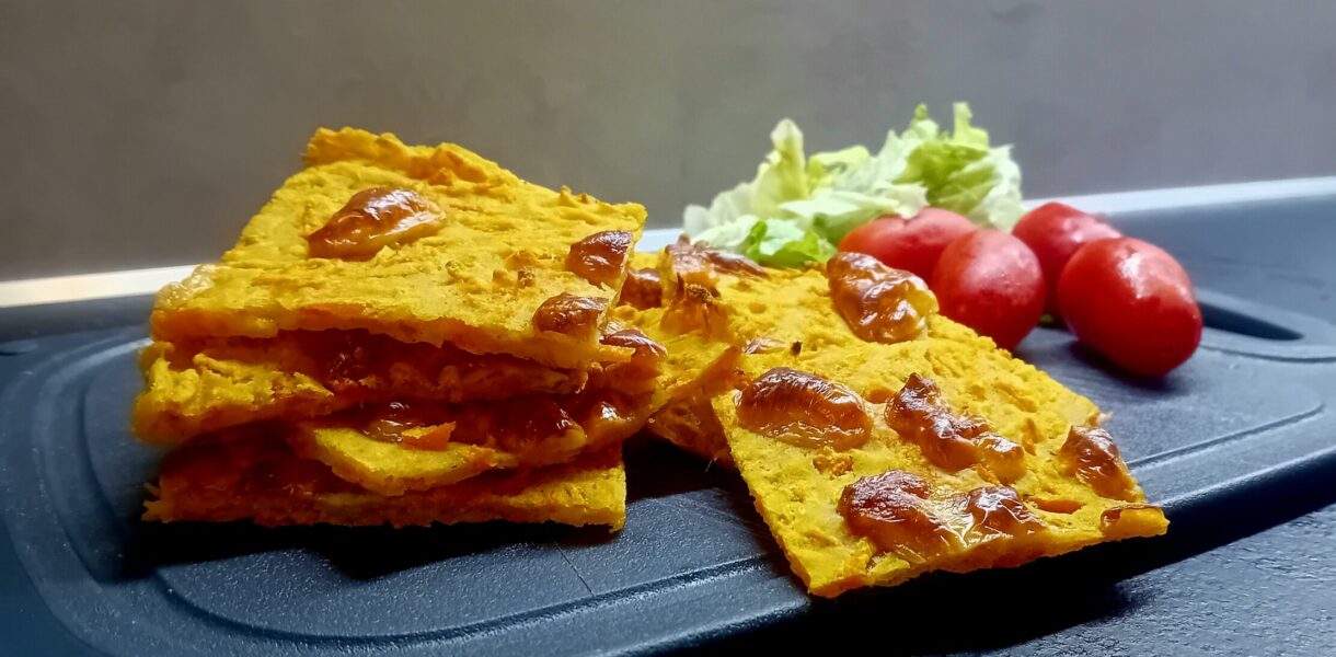 Schiacciata di carote dorata e croccante con sopra pezzetti di scamorza, accompagnata da pomodorini datterini e insalata