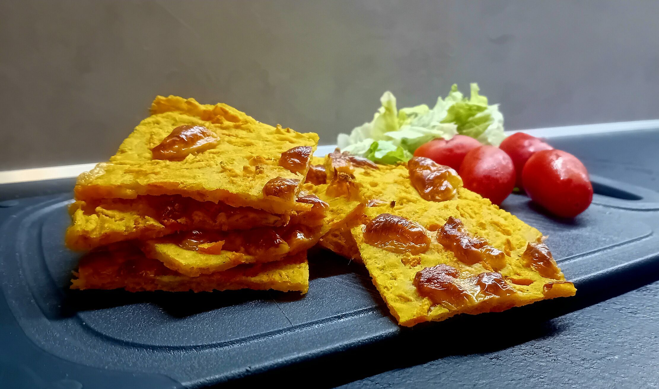 Schiacciata di carote dorata e croccante con sopra pezzetti di scamorza, accompagnata da pomodorini datterini e insalata